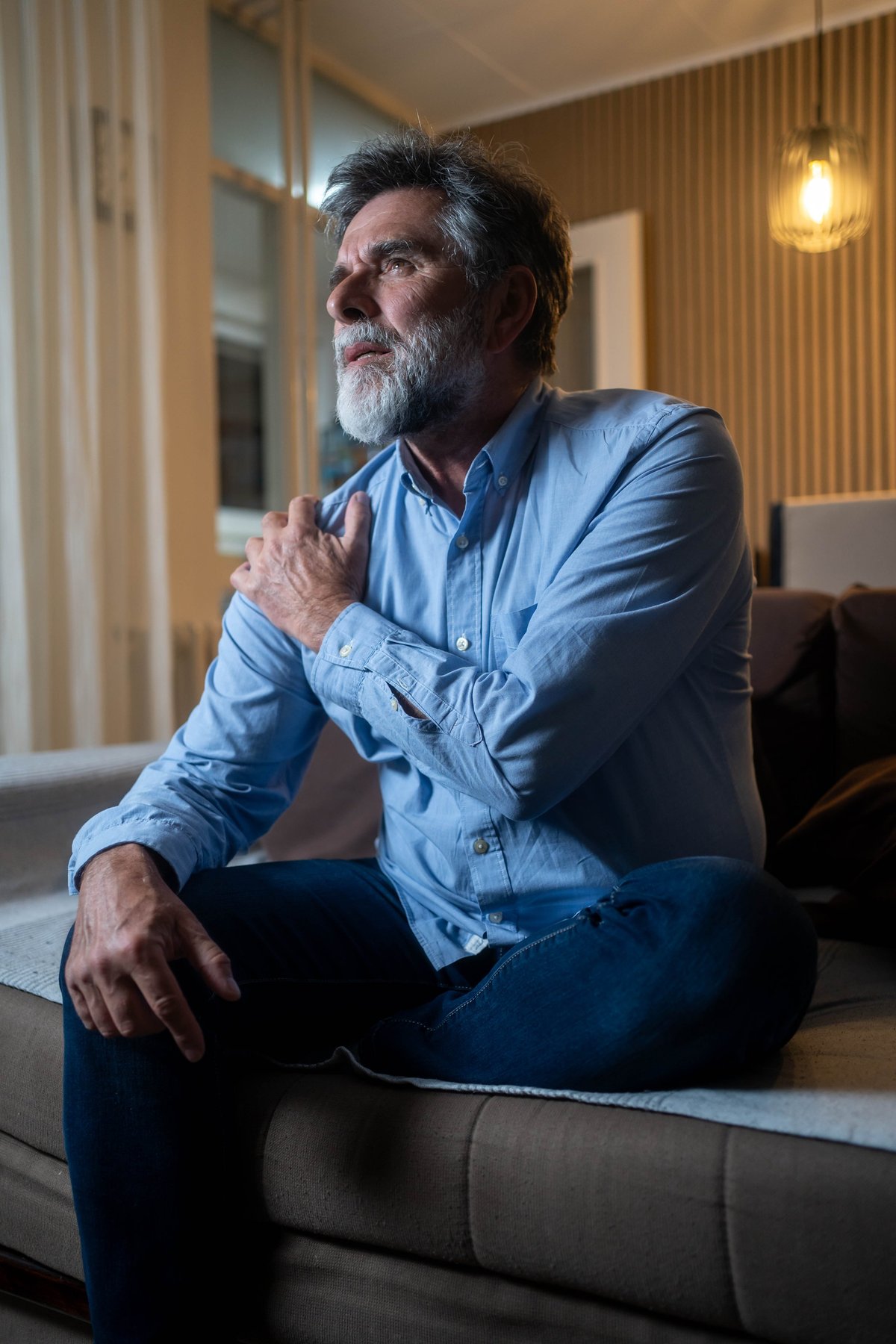 Mature man holding his painful shoulder at home, illustrating shoulder arthritis discomfort