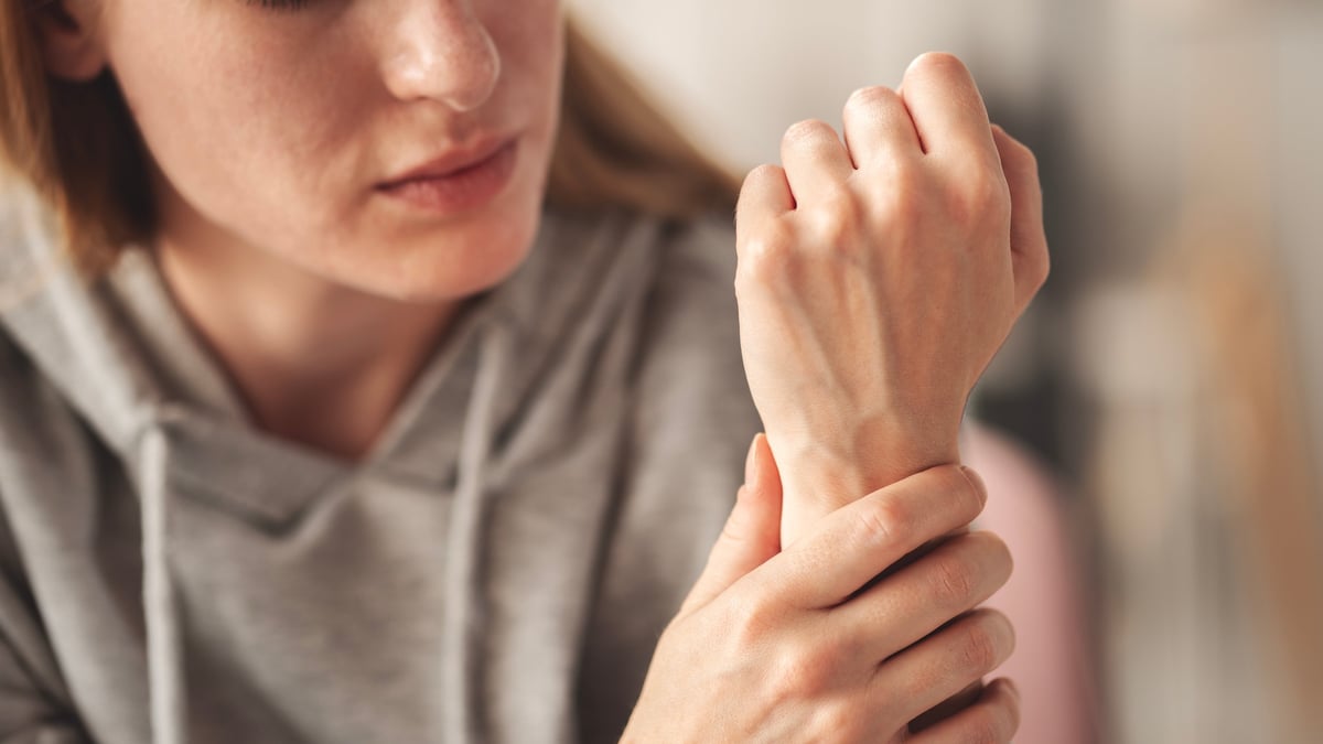 Young woman holding her wrist with an expression of pain and discomfort