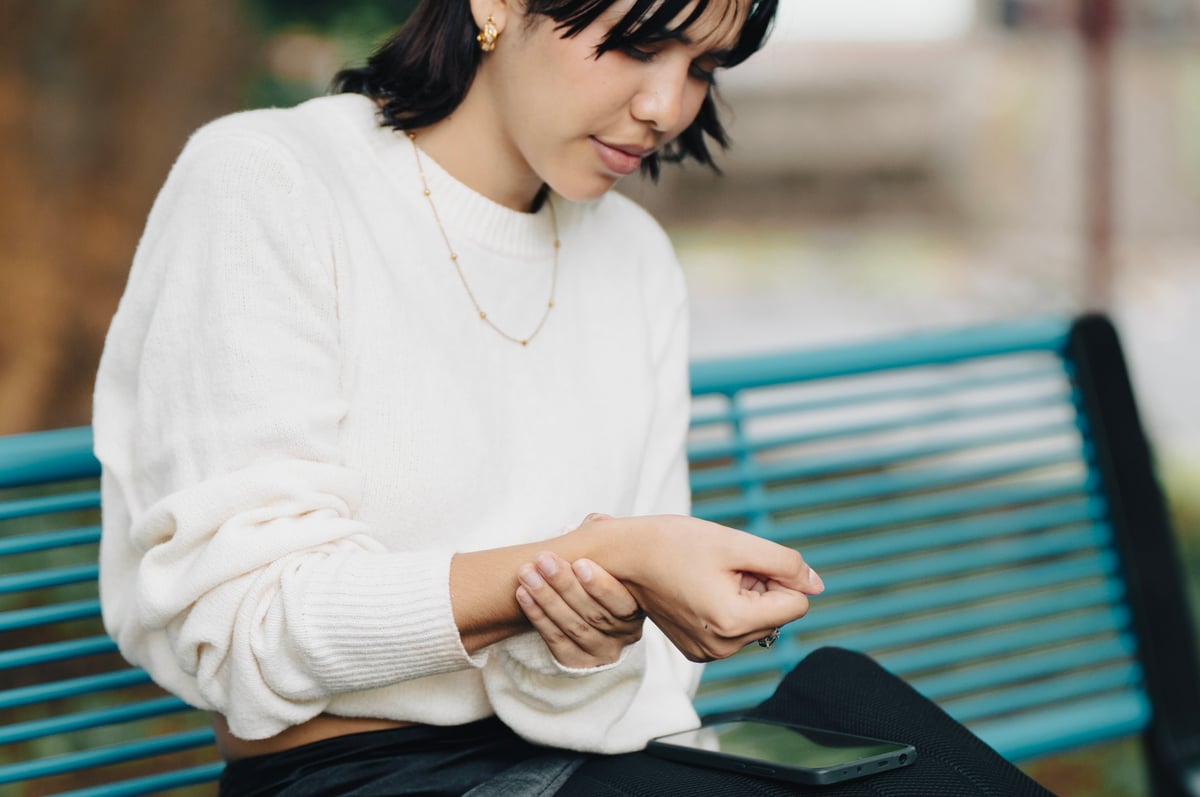 Young woman with wrist pain holding her phone, discomfort at the base of the thumb