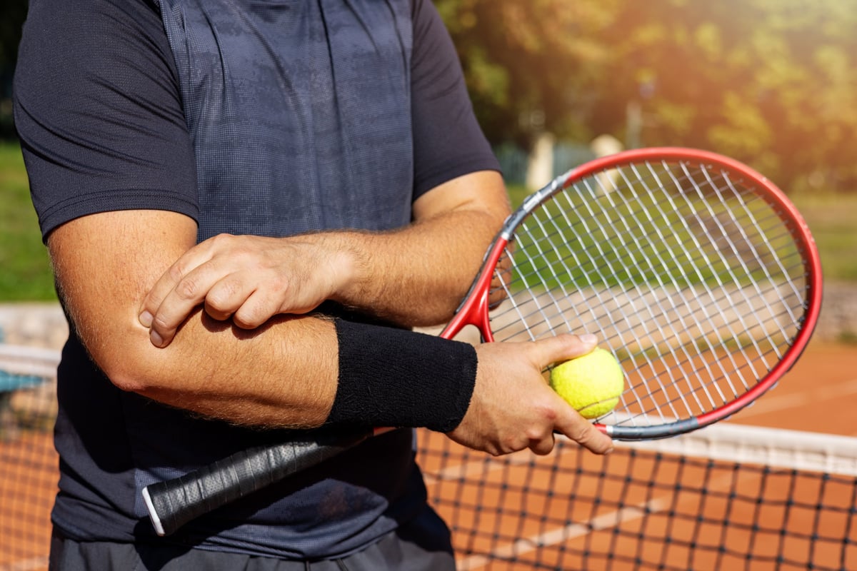 Tennis player holding their elbow in pain during a match, showing tendon strain