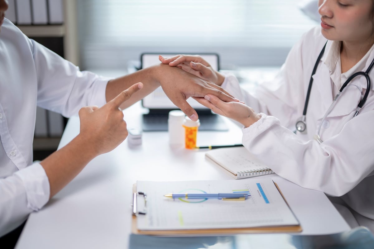 Physician examining the palm of a patient's hand, where Dupuytren's cords and nodules form